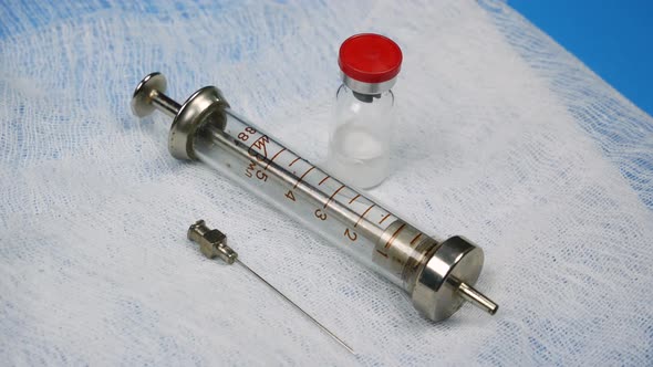 Glass Syringe, Needle and Medicine in Vial Rotating on Blue Background