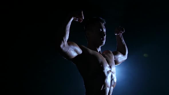 Asian Muscular Man Shows Demonstrates Muscles. Black Background. Slow Motion . Silhouette