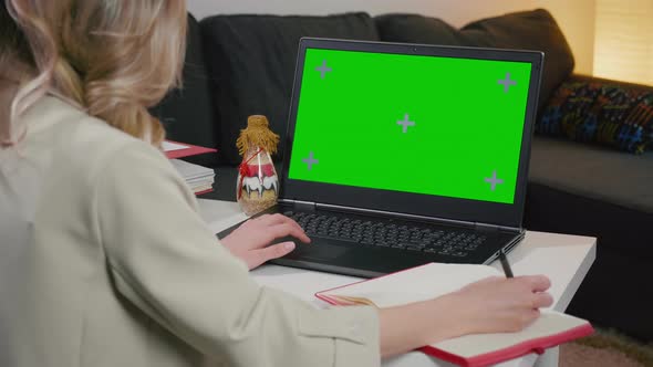 Chromakey Mockup. Woman writing and using laptop with blank green screen.