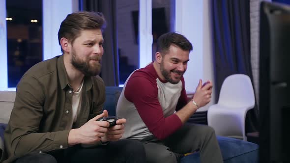 Guys Sitting on the Couch and Playing Video Games on TV Using Gamepads