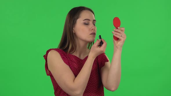 Portrait of Tender Girl in Red Dress Is Painting Her Lips Looking in Red Mirror. Green Screen