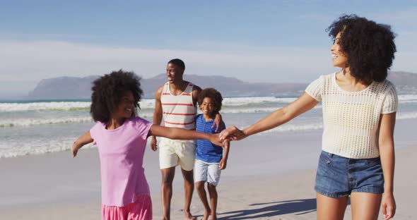 Smiling african american parents and their children walking holding hands and embracing on the beach