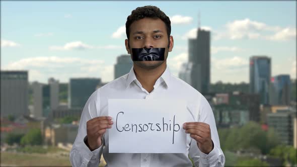 Indian Man with Taped Mouth on Cityscape Background