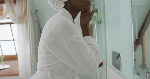 African american attractive woman applying face cream in bathroom