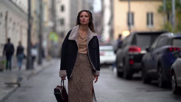 Young Woman Listening To Music with Headphones and Enjoying Walking in the City Outdoors. It Is