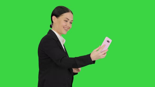 Young Female in a Suit Having Business Video Call on Her Phone on a Green Screen, Chroma Key.