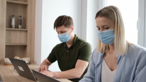 Caucasian Young Couple with Medicinal Mask on Face Are Working at the Laptop.