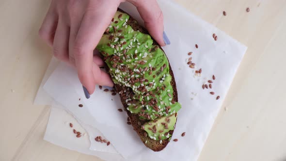 Female hand taking Healthy avocado toast on wooden board. Sesame and flax seeds. Vegetarian food.