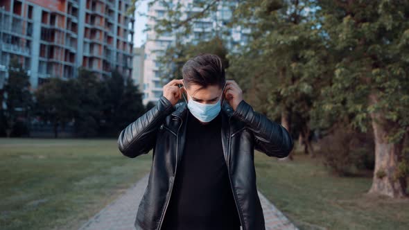 Handsome Young Man Sitting Outdoors and Wearing a Medical Mask To Protect Others From