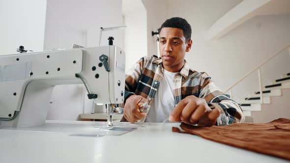 Close Up of African American Man Tailor Finishing Sewing Clothes on Sewing Machine Cutting Thread