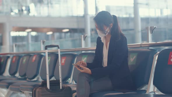 Asian business lady traveller wear suit sitting with suitcase and use smart phone chat message.