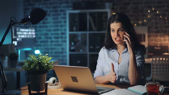 Angry Young Lady Speaking on Cellphone in Office at Night Discussing Problems