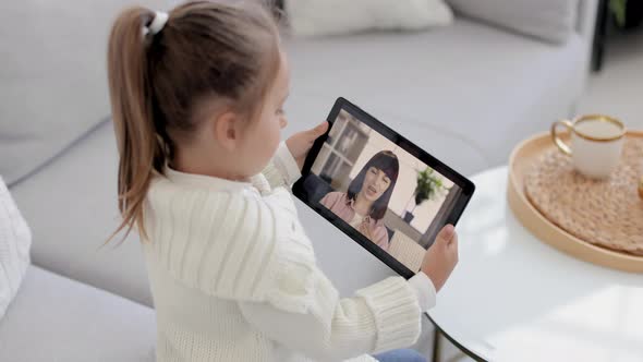 Back View of Young Girl Sitting and Relaxing on Sofa at Home and Talking on Video Call with Smiling