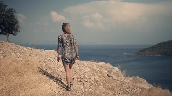 Woman Walking On Sea Cliff.Girl In Dress Walks Under A Rock On Mediterranean Region
