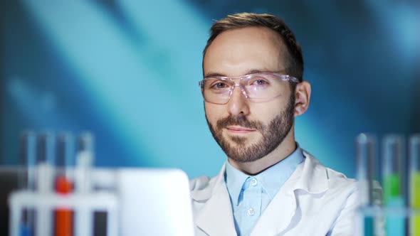 Medium Closeup of Smiling Male Scientist Wearing Glasses and White Coat Using Laptop in Lab