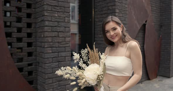 Happy Elegant Young Woman with Flowers in the City