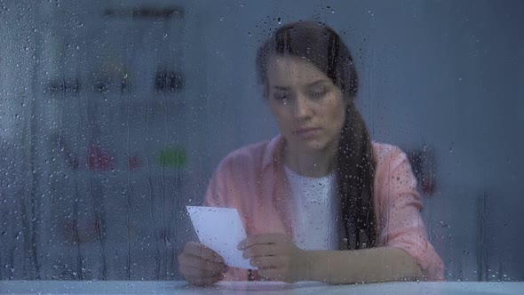 Upset Woman Looking at Photo Behind Rainy Window