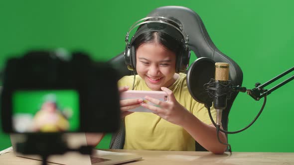 Excited Asian Kid Girl Playing Video Game With Mobile Phone While Live Stream On Green Screen