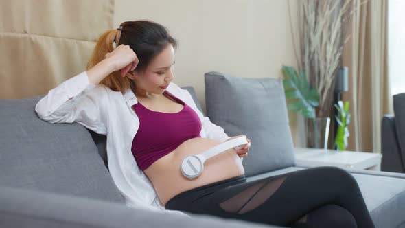 Asian young beautiful pregnant woman applying headphones on her belly.