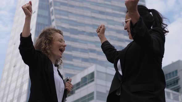 Two Business Ladies Give Each Other a High Five and Join in a Cheerful Hug Celebrating Their Success