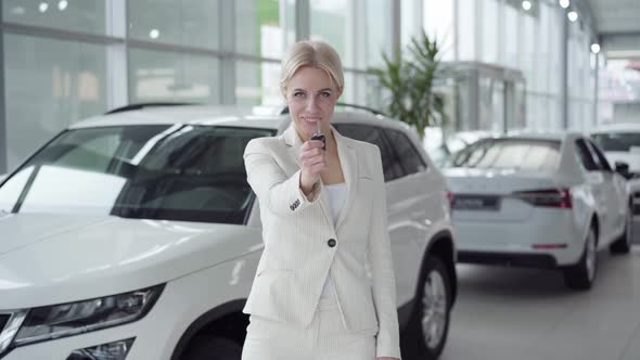 Confident Young Blond Woman Showing Car Keys at Camera and Smiling. Businesswoman in White Suit