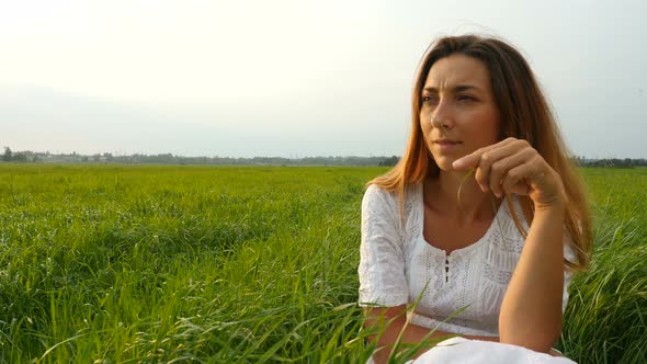 Cute Girl Sitting on the Green Grass and Dreaming. Beautiful Woman Enjoying Nature in Summer Evening