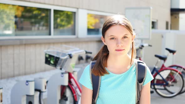 Portrait of inexpressive fifteen-year-old girl by city bikes who then smiles