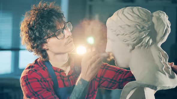 Male Artist in Glasses is Brushing a Gypsum Bust