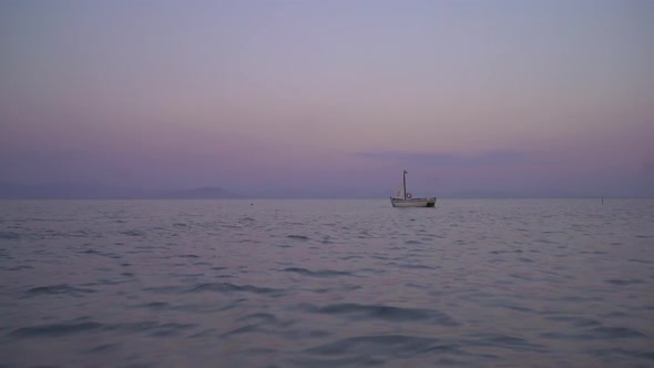 Small sailing boat floating in the ocean in sunset. wide shot revealing mountains in the background