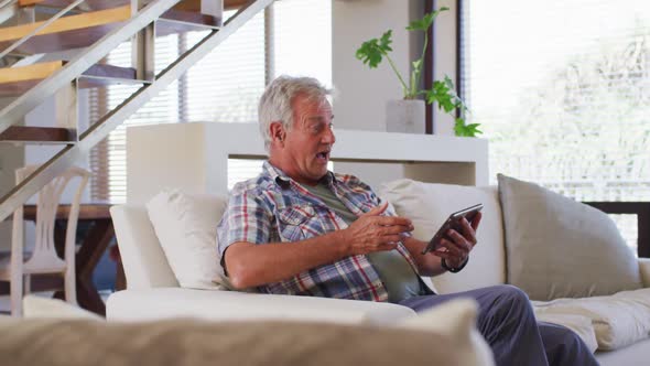 Senior caucasian man having a video chat on digital tablet while sitting on couch at home