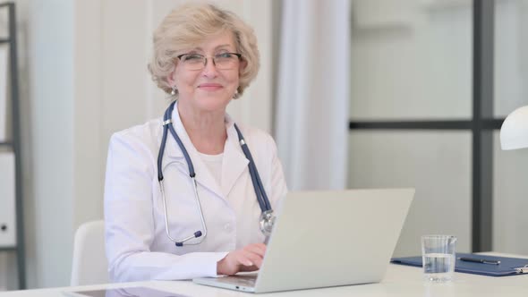 Old Female Doctor with Laptop Smiling at the Camera