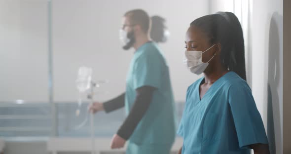 Exhausted African Nurse Leaning on Hospital Corridor Wall and Removing Safety Mask