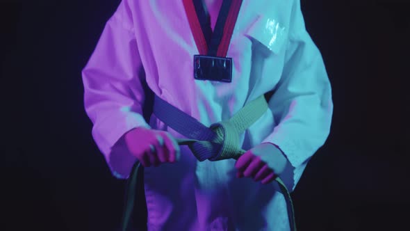 A Little Boy Doing Taekwondo in Neon Lighting  Tying Up His Green Belt and Looks in the Camera