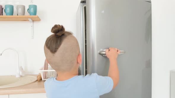 Teenage Boy Opens the Refrigerator in the Kitchen