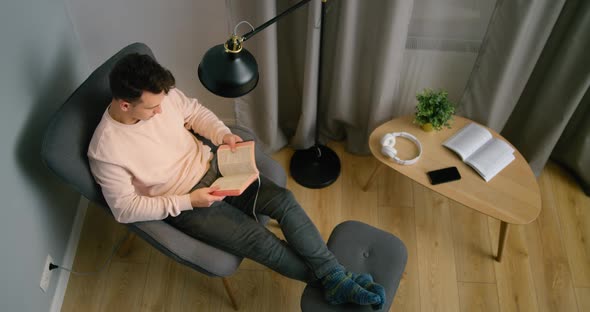 Top View of Christian Man Reading Holy Bible in Armchair at Home at Night