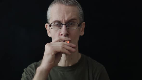 Caucasian Man in Glasses Smokes a Cigarette on a Black Background