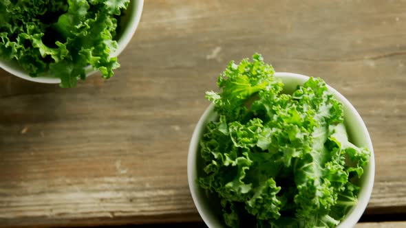 Green lettuce leaves in bowl placed on wooden table 