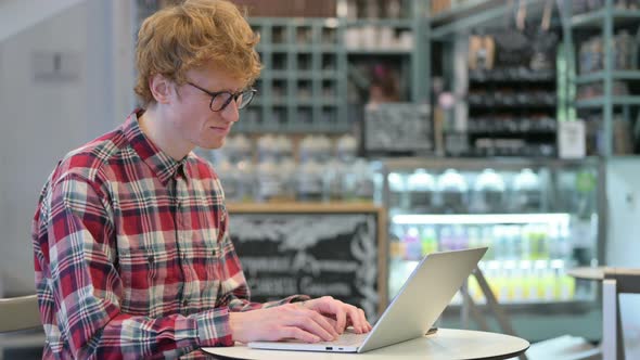 Young Redhead Man Reacting To Loss on Laptop in Cafe 