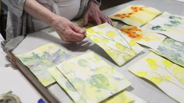 Artist showing off her work at a table and explaining it to the people around her.