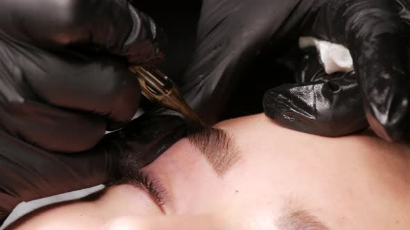 Master Applies Dark Coloring Pigment to Correct Shape of Eyebrows with a Special Machine
