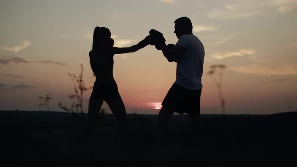 Woman in Gloves Trains Boxing with Man on Background of the Sunset Side View