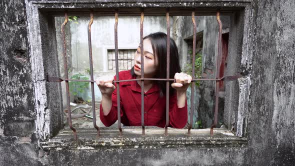 Ethnic woman looking through window with metal grid in old house