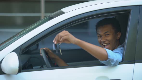 Happy Teenager Showing Car Key to Window Sitting on Driver Seat of New Vehicle