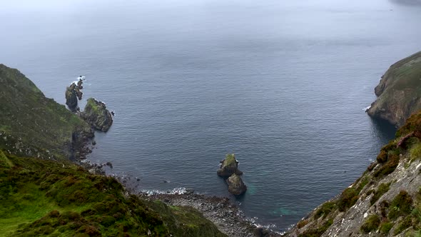 Top down shot of idyllic steep green cliffs in Ireland during foggy and rainy day - Panning shot of