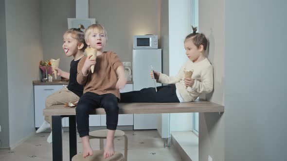 Young Best Friends Kids Sit on Table and Eat Icecream Together in Kitchen at Home