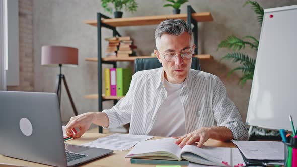 Middle Aged Professor Preparing for Online Lesson with Students Reading Book and Making Notes