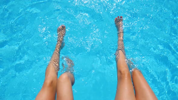 Young Women Sitting on Edge of Pool and Dangling Their Feet in Water. Two Girls with Slim Tanned