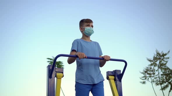 A teenage boy in a medical mask plays sports on exercise machines
