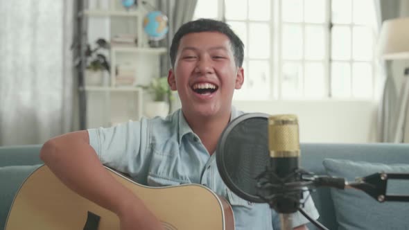 Happy Asian Boy With Guitar And Microphone. The Child Is Broadcasting Live On The Internet