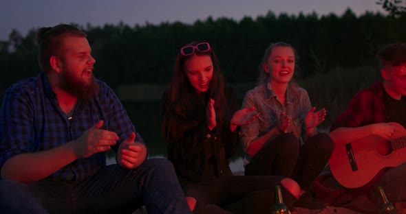 Handsome Teenage Boy is Playing the Guitar While Her Friends are Singing Funny Songs and Laughing